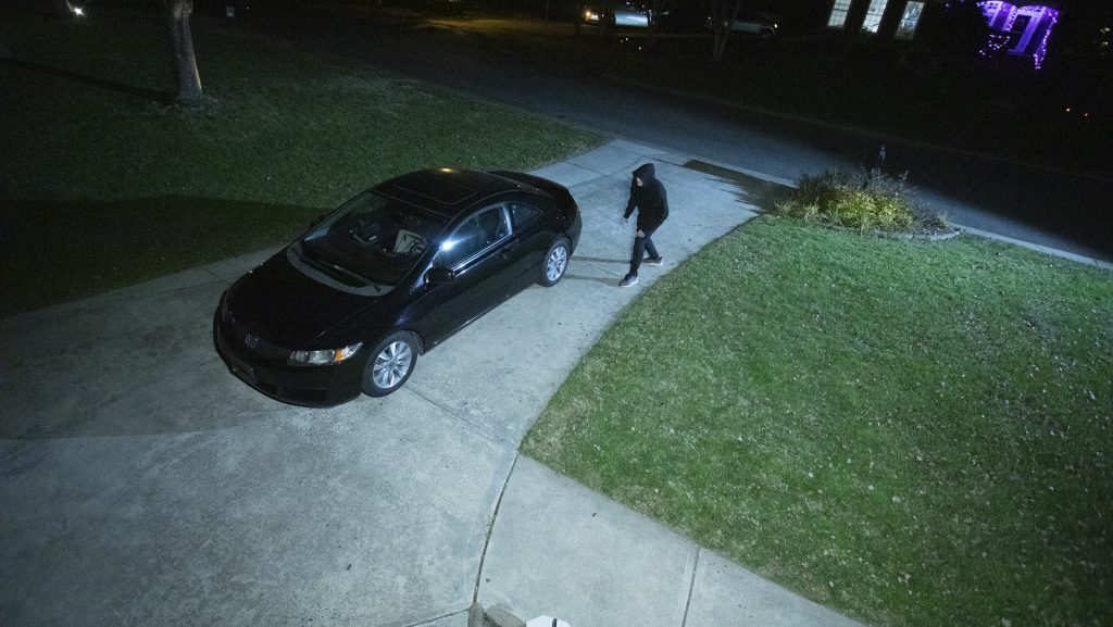 20231106tb_8360_eml_1080 Man dressed in black standing outside a sedan in a home’s driveway at night
