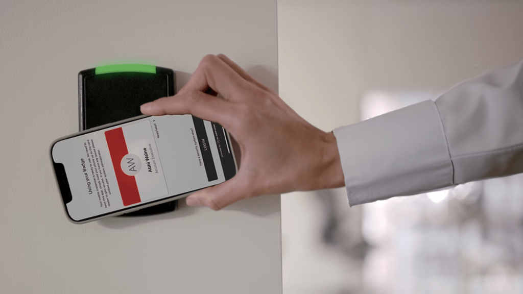 Person holding a smartphone up to a black access control box to unlock a door in a commercial building