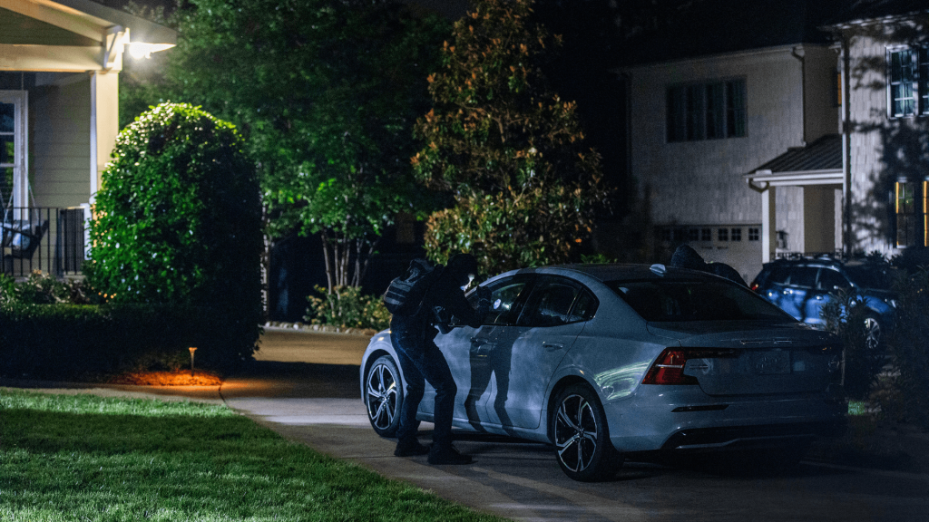 Man dressed in black standing outside a white sedan in a home’s driveway at night