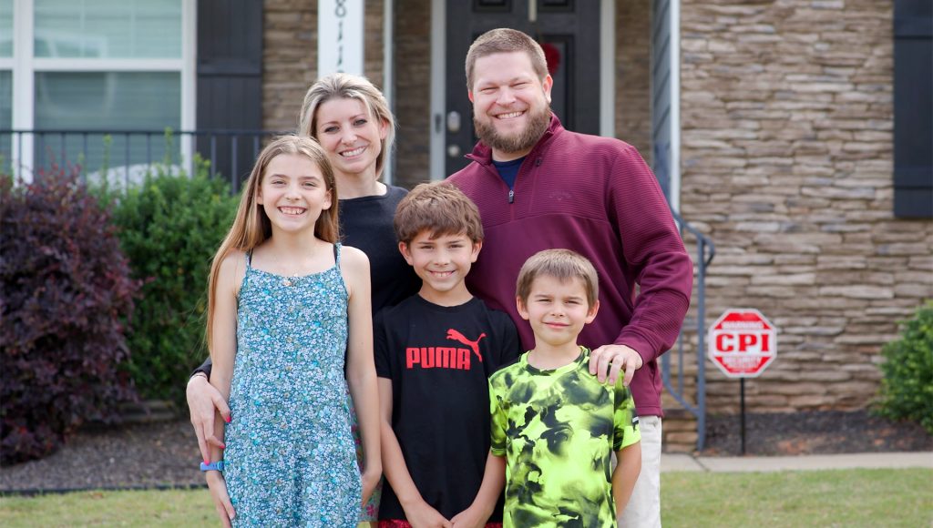 Family posing for photo in front of house with cpi security sign