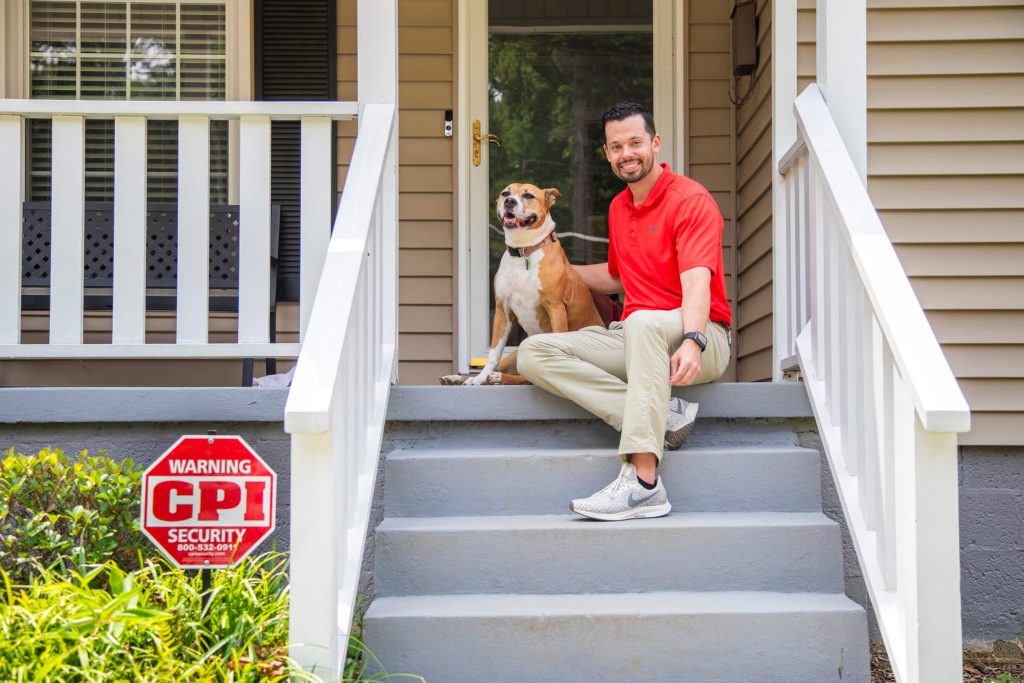 Man sitting with dog on front porch next to CPI Security sign