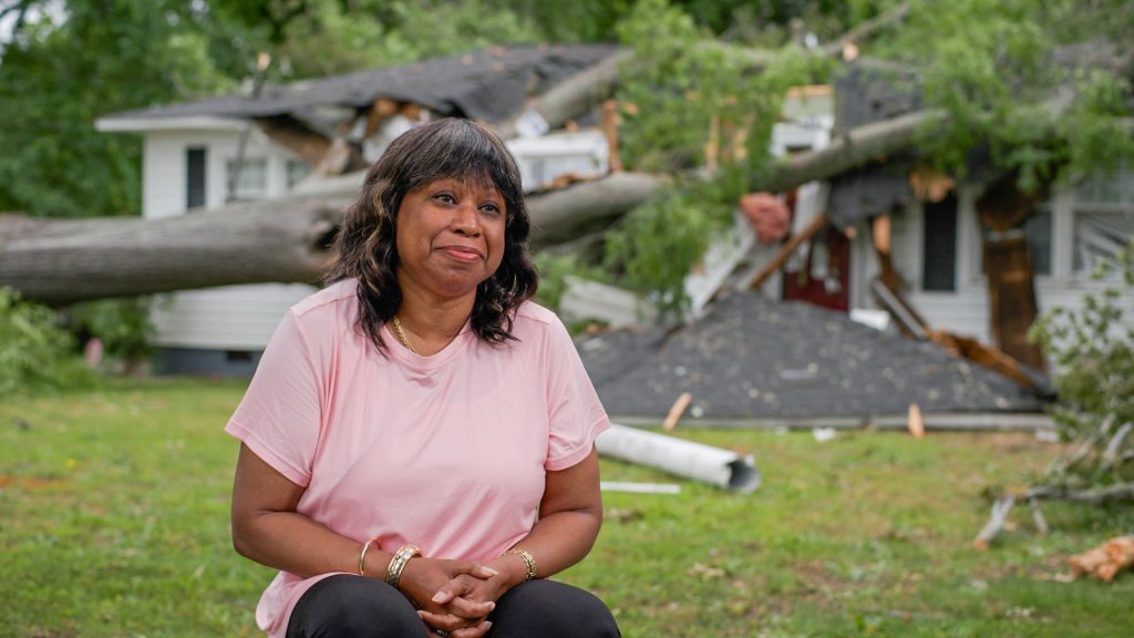 Devery Davis in front of crushed home being interviewed
