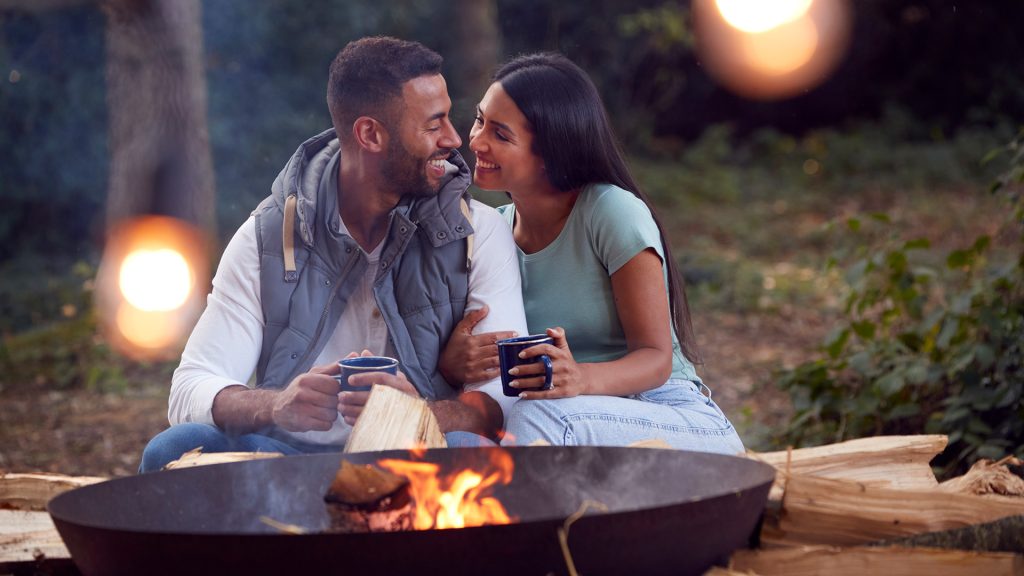 Couple embracing next to camp fire and drinking cocoa