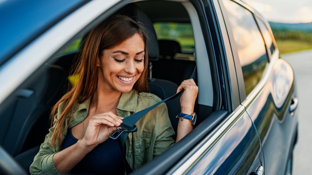 Woman putting on seat belt in car
