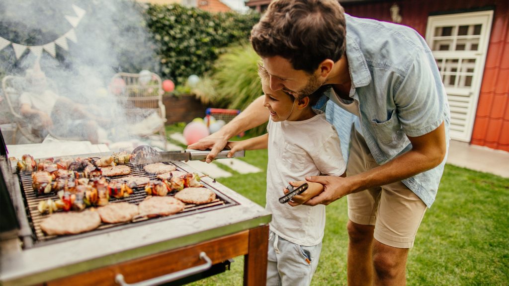 Dad showing son how to grill meats outside