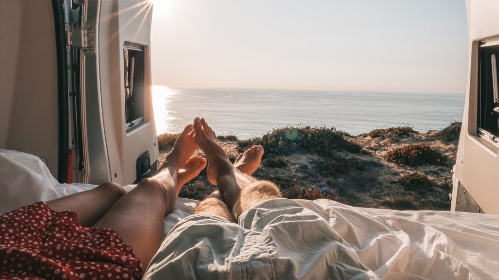 Two people lounging in camper van looking out at the ocean