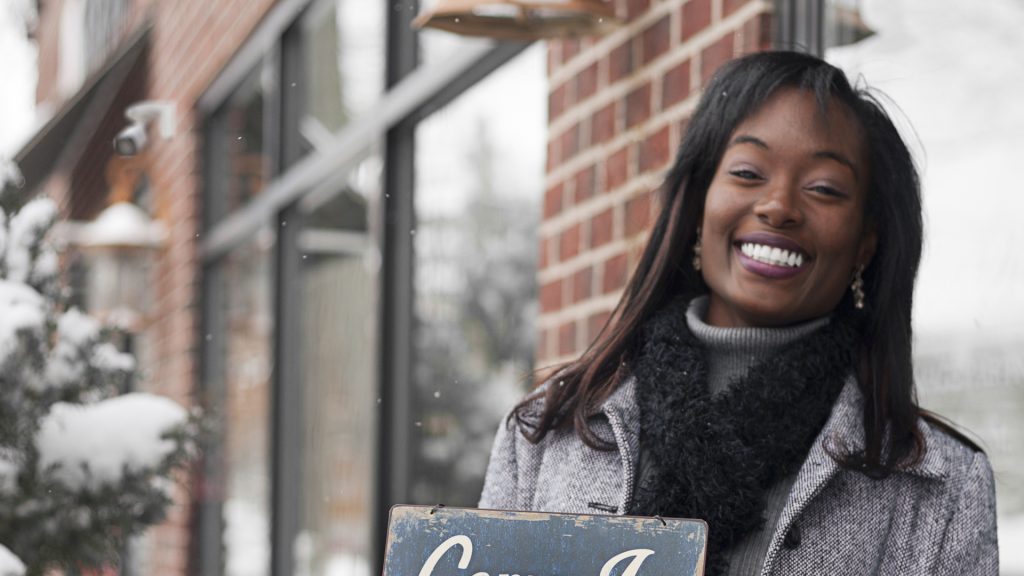 Business owner in the snow holding sign that says "Come in we're open"