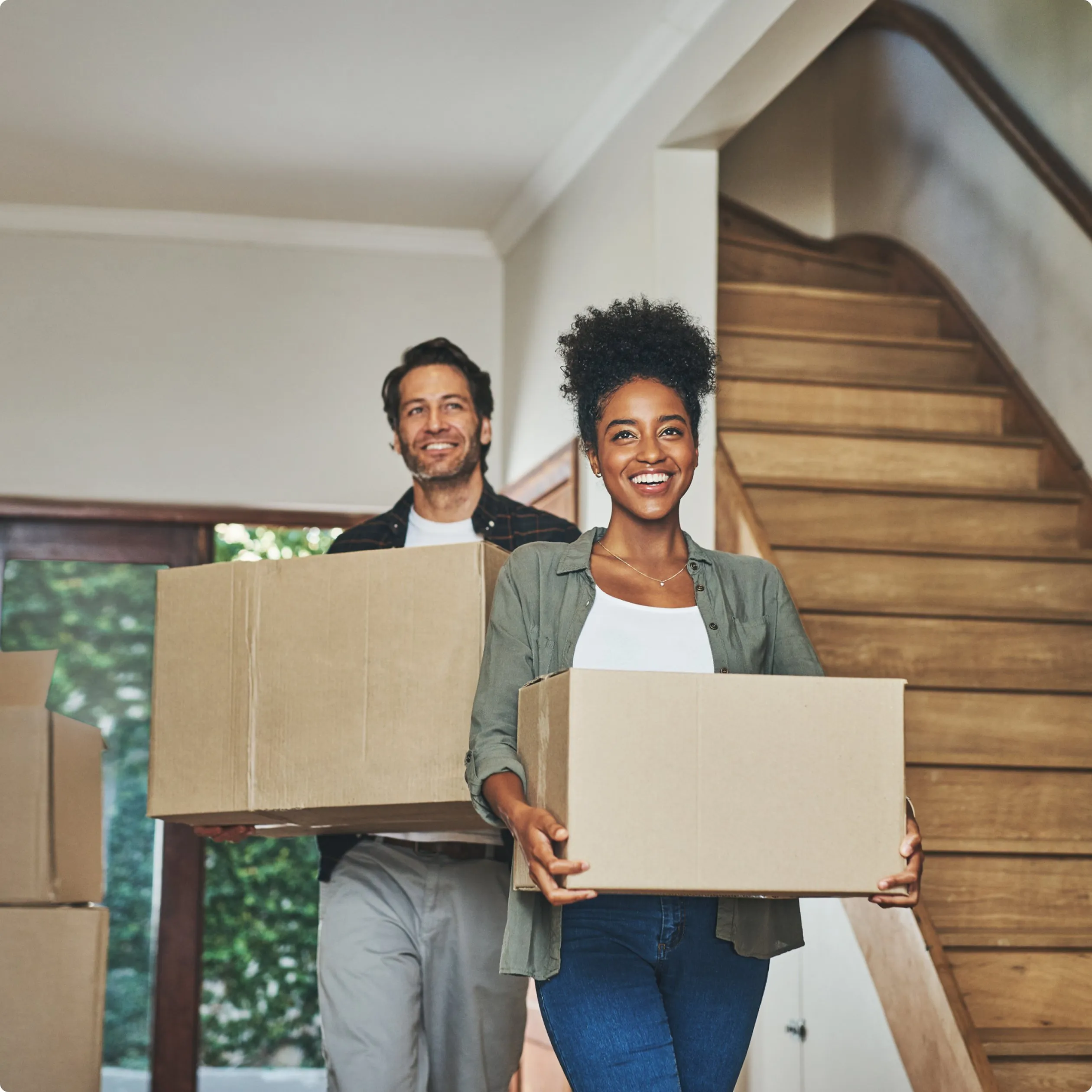 activate_mobile-hero Man and woman walking down a hallway of a house, each carrying a box, with stairs visible in the background