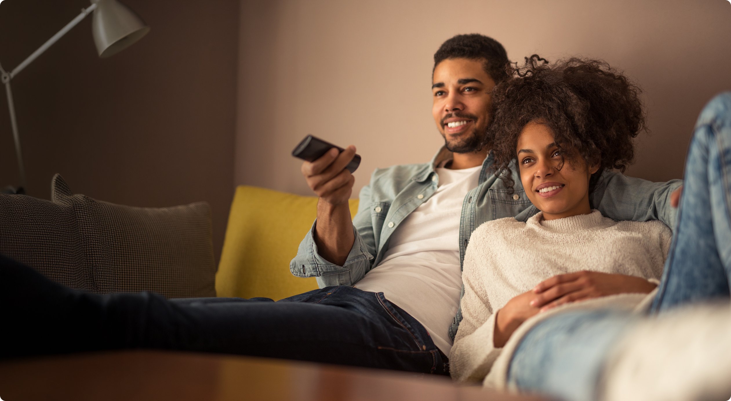 Happy couple cuddling on a couch, with the man holding a remote