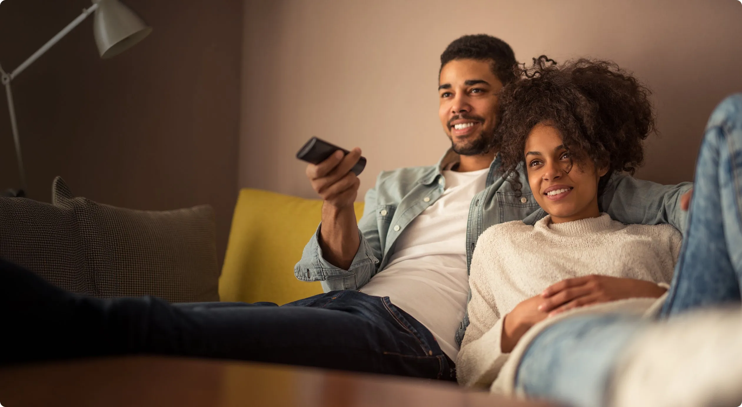 Happy couple cuddling on a couch, with the man holding a remote