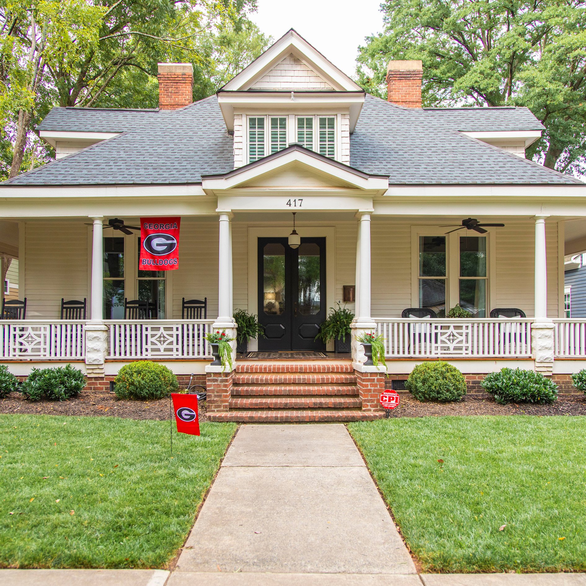 White Craftsman-style house displaying Georgia Bulldogs flags and a CPI Security sign in the yard