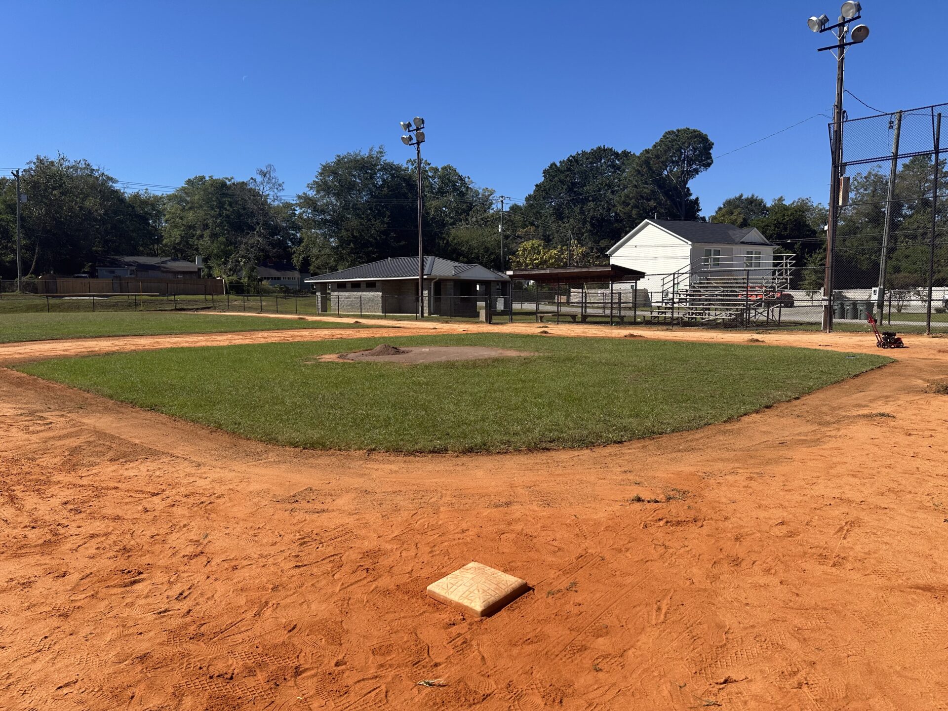 Small rural baseball field with dug out and bleachers in background