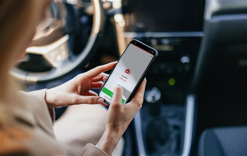 Woman using a home security app on her smartphone to arm her system while sitting in her car